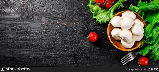 Mozzarella cheese with cherry tomatoes and lettuce. On a black background. High quality photo. Mozzarella cheese with cherry tomatoes and lettuce.