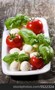 mozzarella, green basil and tomatoes on wooden table