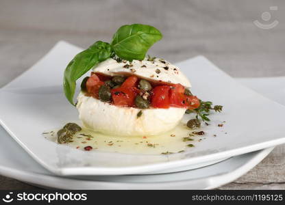 Mozzarella stuffed tomatoes with capers, seasoned spices and basil in oil