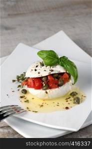 Mozzarella stuffed tomatoes with capers, seasoned spices and basil in oil