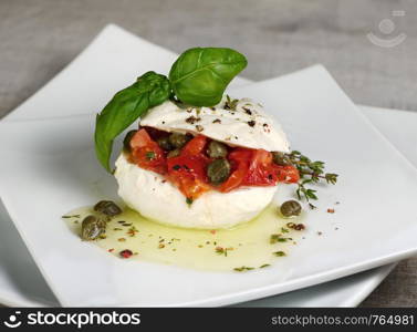 Mozzarella stuffed tomatoes with capers, seasoned spices and basil in oil