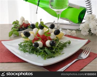 Mozzarella with cherry tomatoes and olives on a skewer with arugula and white wine