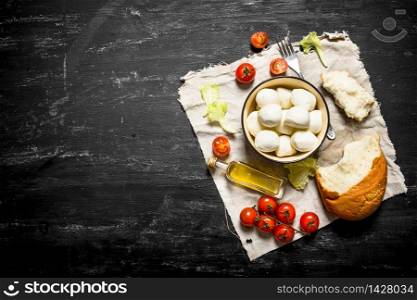 Mozzarella with fresh bread, tomatoes and greens. On a black wooden background.. Mozzarella with fresh bread, tomatoes and greens.