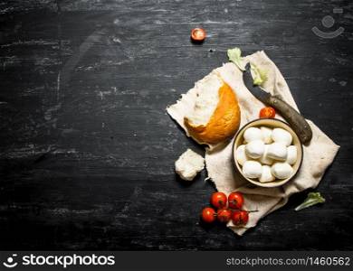 Mozzarella with fresh bread, tomatoes and greens. On a black wooden background.. Mozzarella with fresh bread, tomatoes and greens.