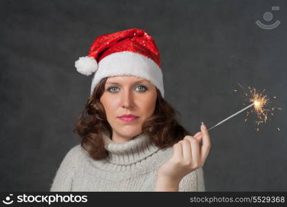 mrs Santa with blank expression studio shot. Cute girl in Santa hat holding sparklers