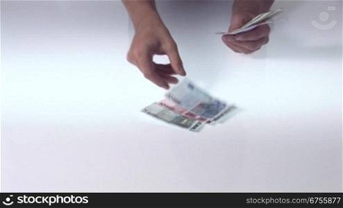 MSnnerhand zShlt einen FScher Geldscheine auf eine Tischplatte.