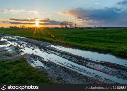 Muddy road with puddles, green field and sunset, Czulczyce, Lubelskie, Poland