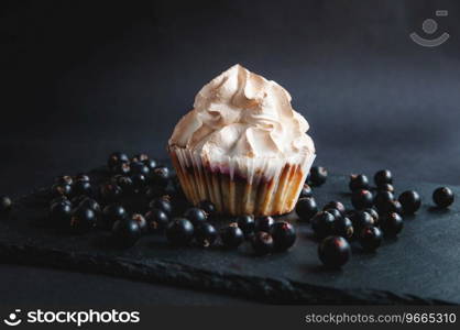 Muffin on a black background with currant berries. On a dark background, cakes with fruit filling and berries and currants on a black stone serving board.
