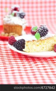 muffin with whipped cream, cake with icing, raspberry, blackberry and mint on a plate on plaid fabric