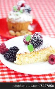 muffin with whipped cream, cake with icing, raspberry, blackberry and mint on a plate on plaid fabric