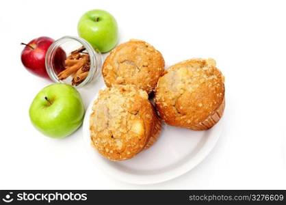 Muffins On A Saucer. Apple spice muffin with red and green apples and stick cinnamon in the background isolated on white