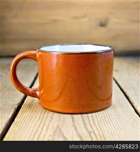 Mug is brown with a drink on the background of wooden boards