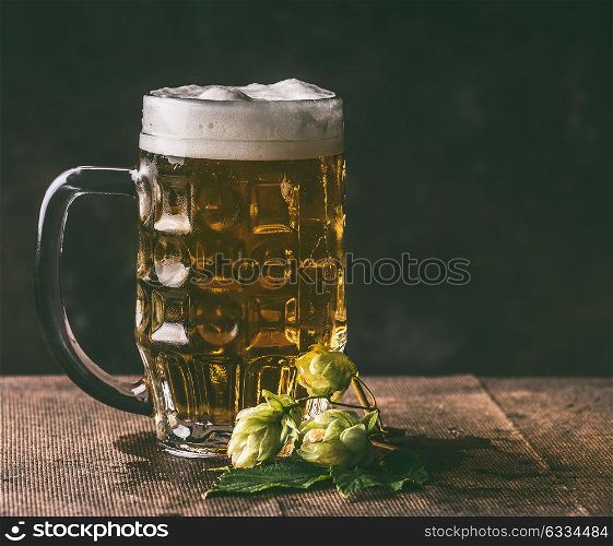 Mug of beer and hops on dark rustic table background, front view, copy space. German style