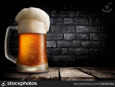 Mug of beer on table near black brick wall