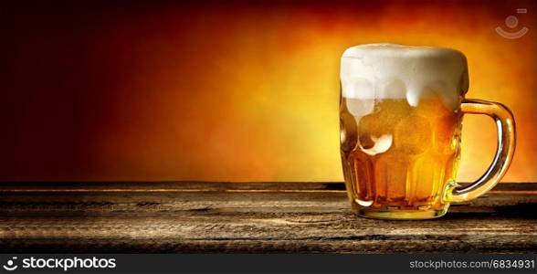 Mug of beer on timber table and orange background