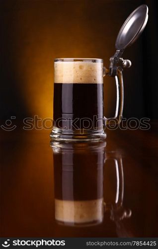 Mug of dark beer over a dark background lit yellow