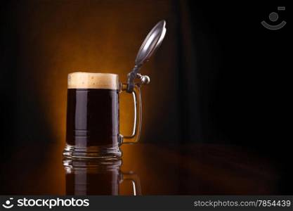 Mug of dark beer over a dark background lit yellow