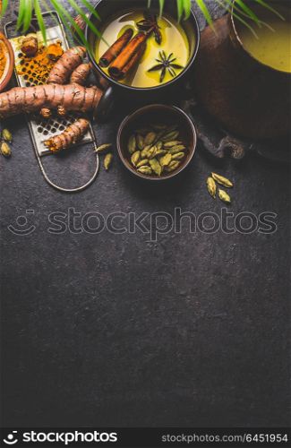 Mug of healthy turmeric milk drink with ingredients: fresh turmeric roots , spices and honey on dark background, top view. Hot winter beverage. Immune boosting remedy , detox and dieting concept