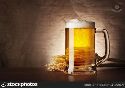 Mug of lager beer with spikelets on burlap background