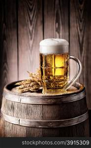 Mug of light beer with foam and spikelets on a wooden barrel. Mug of light beer with foam and spikelets