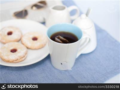 Mug of Tea, Cookies, Cream Pot, Sugar Basin and Newspapers with Glasses on Table