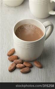 Mug with hot chocolate milk and whole cocoa beans