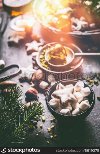 Mug with marshmallows and cinnamon star Christmas cookie on dark rustic table with nuts , chocolate and fir brunches.
