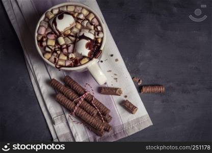 Mug with milk chocolate and marshmallows on top. Chocolate sticks tied with red-white string. Directly above view with copy space
