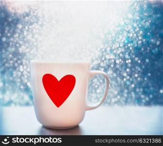 Mug with red heart and bokeh at blue background, close up, front view. Layout of greeting card for Mothers day, Valentines day or birthday. Love concept