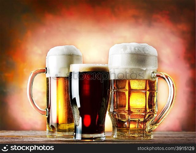 Mugs and glass of beer on a wooden table on a red background. Mugs and glass of beer on a wooden table