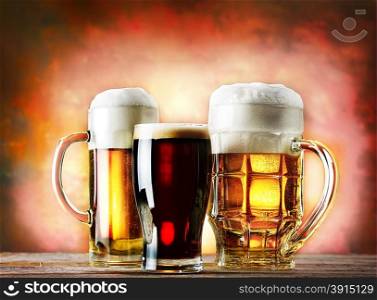 Mugs and glass of beer on a wooden table on a red background. Mugs and glass of beer on a wooden table