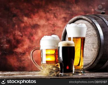 Mugs and glasses with light dark beer on background wooden barrel. Mugs and glasses with light dark beer