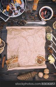 mulled wine and ingredients in iron spoons for making a drink on a brown wooden background, in the middle mashed brown kraft paper for writing a recipe, top view