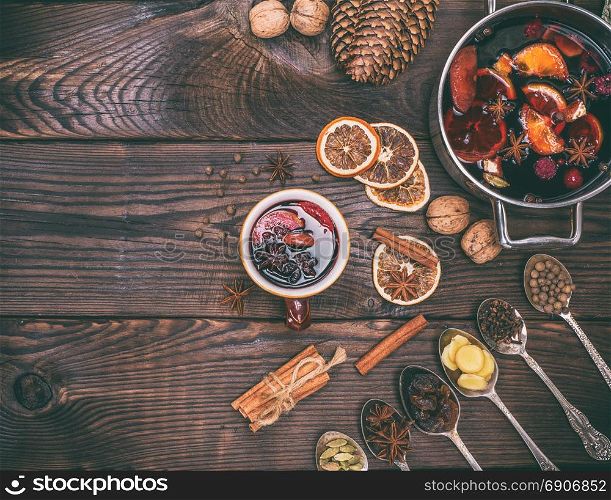 mulled wine and ingredients in iron spoons for making a drink on a brown wooden background, empty space on the left