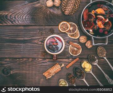 mulled wine and ingredients in iron spoons for making a drink on a brown wooden background, empty space on the left