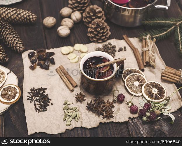 mulled wine in a brown ceramic cup on a brown sheet of paper with ingredients: cinnamon, cardamom, cloves, orange, sugar, ginger and star anise