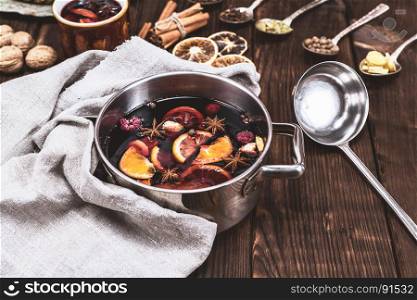 mulled wine in a pan with an iron scoop, behind the ingredients in spoons on a brown wooden background