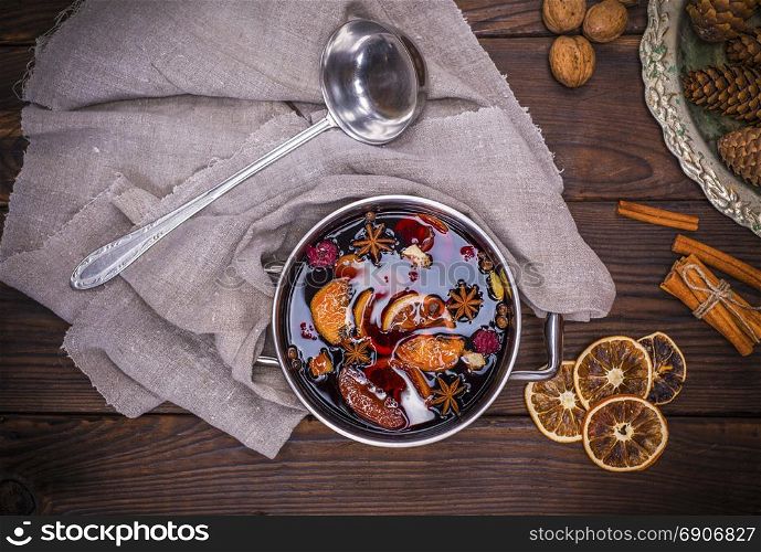 mulled wine in a pot with handles and ingredients for making a home made alcoholic drink on a brown wooden background, top view
