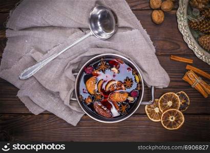 mulled wine in a pot with handles and ingredients for making a home made alcoholic drink on a brown wooden background, top view