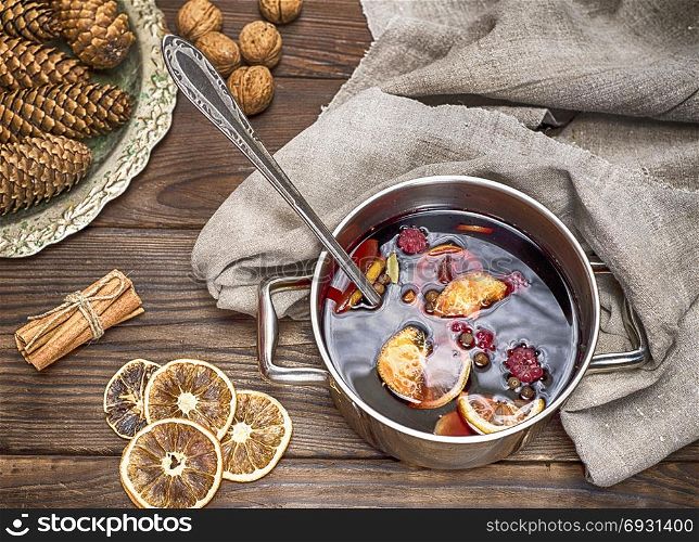 mulled wine in a pot with handles and ingredients for making a home made alcoholic drink on a brown wooden background
