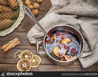 mulled wine in a pot with handles and ingredients for making a home made alcoholic drink on a brown wooden background