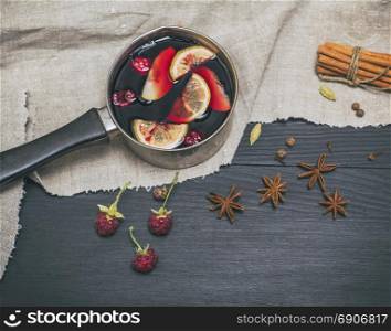 mulled wine in an aluminum ladle on a black wooden background, top view, vintage toning