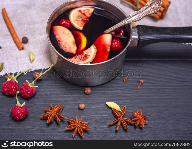 mulled wine in an aluminum ladle with a handle on a black background, top view