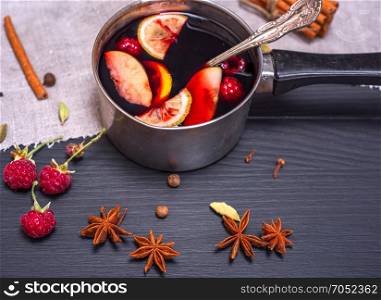 mulled wine in an aluminum ladle with a handle on a black background, top view