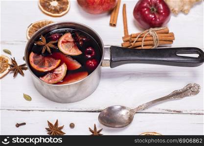 mulled wine in an aluminum ladle with a handle on a white wooden background, top view