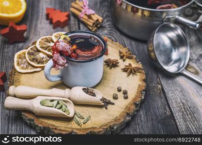 mulled wine in an iron mug and ingredients on a wooden background