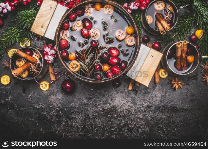 Mulled wine or punch in cooking pot and mugs with ingredients on dark rustic vintage background, top view, border