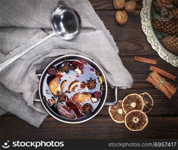 mulled wine with spices and pieces of fruit in a round aluminum pan, next to an iron scoop, top view. mulled wine with spices and pieces of fruit in a round aluminum