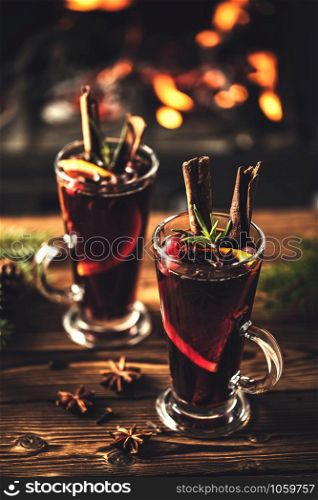 Mulled wine with spices in glasses on a wooden table against the background of a fireplace fire. Winter drink traditional for the Christmas holidays.