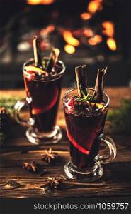 Mulled wine with spices in glasses on a wooden table against the background of a fireplace fire. Winter drink traditional for the Christmas holidays.